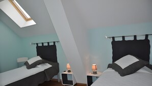Une chambre avec deux lits, une lucarne et des lampes de chevet.