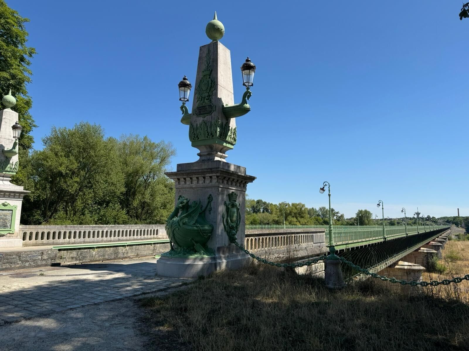 A statue with a green dragon and a pedestal, surrounded by a fence and a bridge.