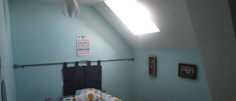 A bedroom with a bed, a ceiling fan, a skylight, a wall-mounted sign, and a small bedside table.