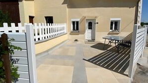 Un bâtiment avec un toit recouvert de tuiles, une clôture blanche et un patio comprenant une table et des chaises.