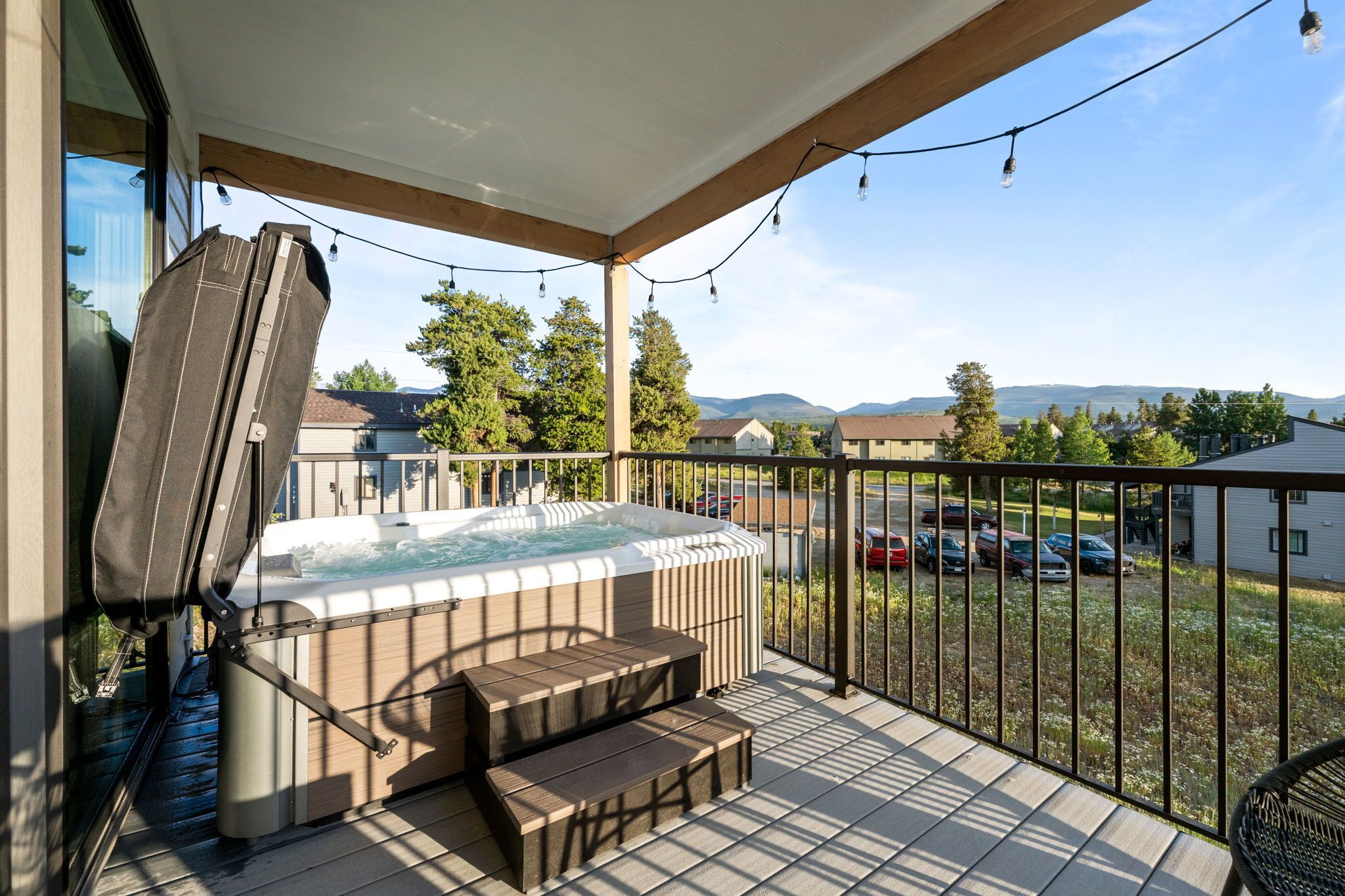 A balcony with a hot tub, wooden steps, and a view of a parking lot and trees.