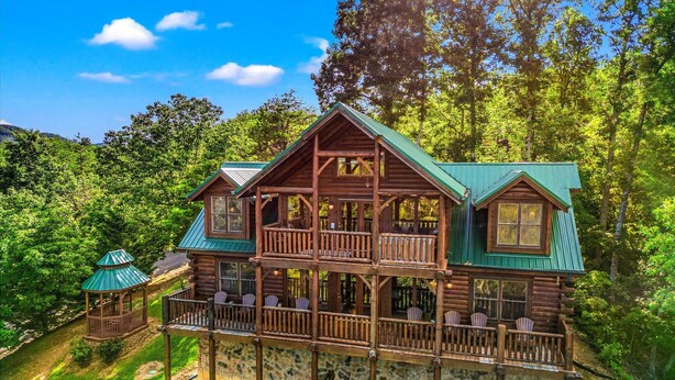Une cabane en rondins dotée d’un balcon et d’un belvédère séparé, le tout entouré d’une végétation luxuriante.