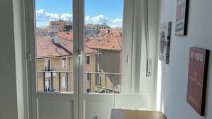 Ein Zimmer mit einem Holztisch und einem weißen Stuhl, ein Fenster mit Blick auf Gebäude und einen klaren Himmel.