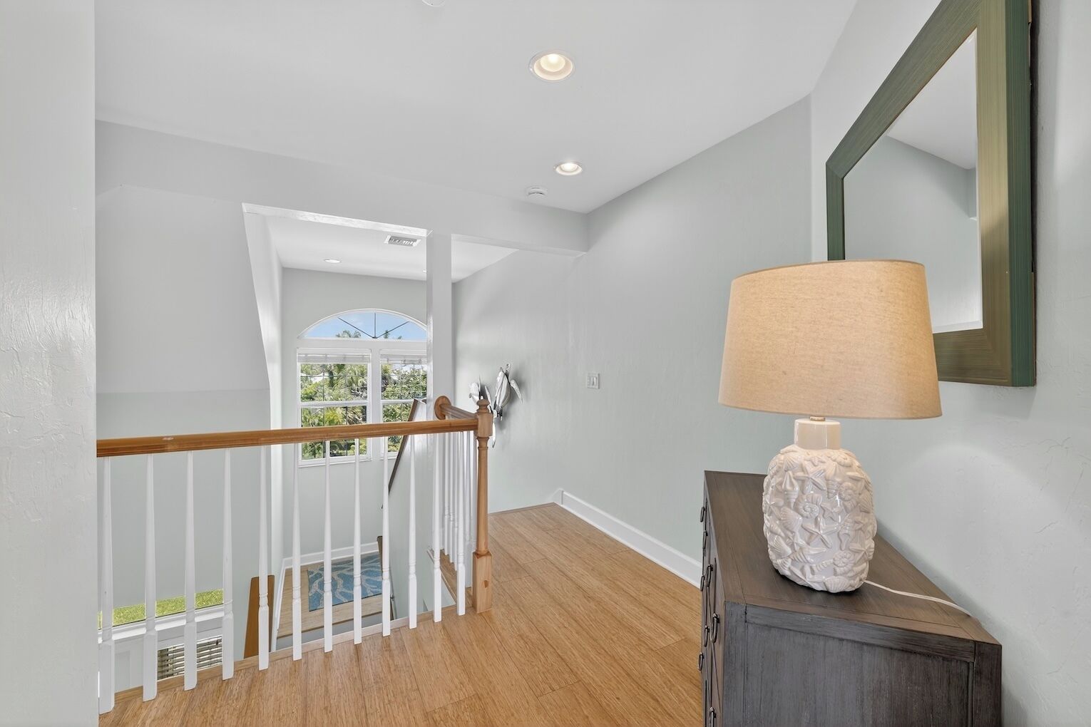 A hallway with a wooden staircase, a white railing, and a lamp on a cabinet.