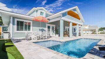 A modern house with a swimming pool, outdoor seating, and a covered patio area.