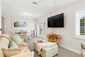 A modern living room with a sofa, ottoman, and a flat-screen TV mounted on the wall.