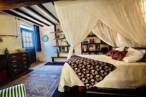 A bedroom with a canopy bed, a wooden dresser, a patterned rug, and a bookshelf with various items.