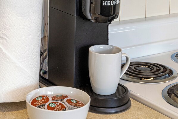 A kitchen with a coffee maker, a white mug, and a bowl of coffee pods.