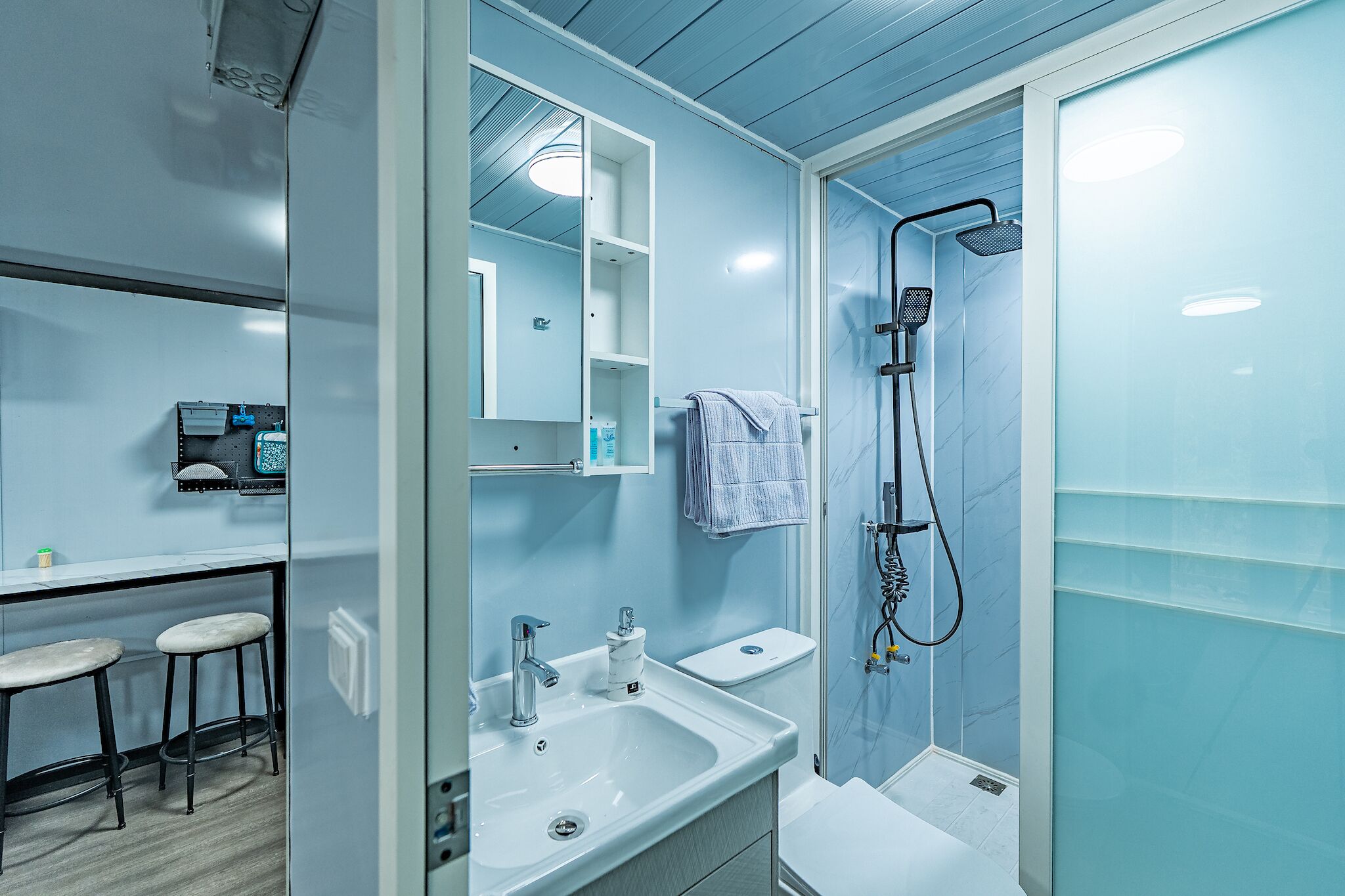A modern bathroom with a shower, sink, and two stools.