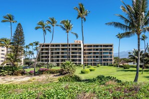 A hotel with a multi-story structure, surrounded by palm trees and a well-maintained lawn. - Koa Lagoon #503 Panoramic Ocean View, 1BD/1BA, Sleeps 4 (Kihei)