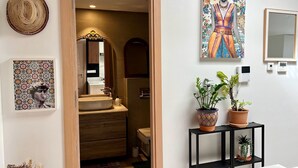 Een moderne badkamer met een vrijstaand bad, een spiegel en een wastafel. Er staan potplanten op een zwarte plank en er hangt kunst aan de muren.