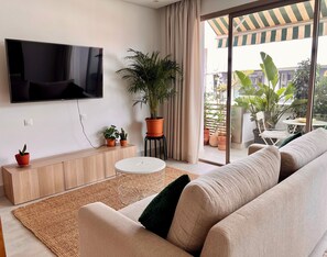 Een moderne woonkamer met een flatscreen televisie, een bank, een salontafel en een grote potplant.