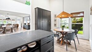 A modern kitchen with a large island, dark cabinetry, and a dining area with a round table and chairs.