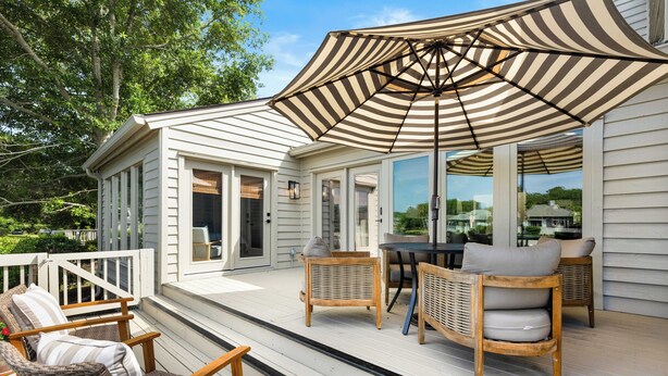 A covered outdoor deck with wicker furniture and a striped umbrella.