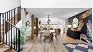 A spacious living area with a dining table, chairs, and a staircase with black railings.
