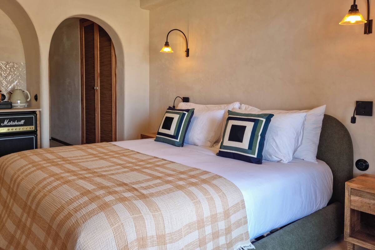 A hotel room with a large bed, two wall-mounted lamps, a wooden arched doorway, and a Marshall amplifier on a table.