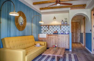 Ein gemütliches Zimmer mit einem gelben Sofa, einem Holztisch, einer karierten Spritzschutzwand und einem Deckenventilator.