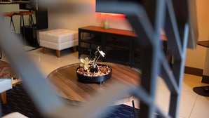 A modern living room with a round wooden coffee table, a white sofa, and a small dining area with a red-lit table.