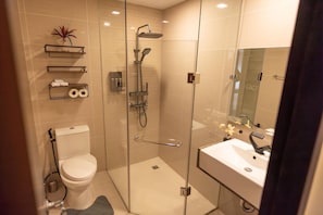 A modern bathroom with a glass-enclosed shower, a toilet, a sink with a mirror, and shelves with toiletries. - Luxury Cozy Stylish Loft in Makati (Makati)