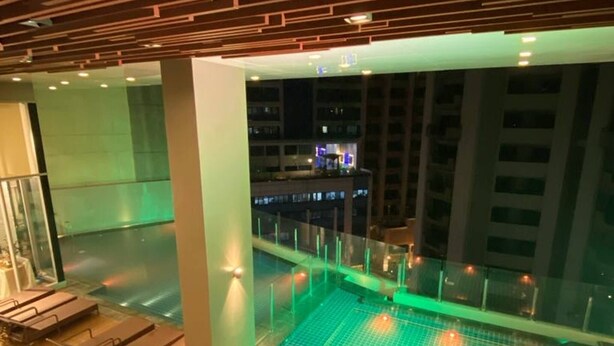 A rooftop pool area with lounge chairs and a dining table, surrounded by a glass railing.