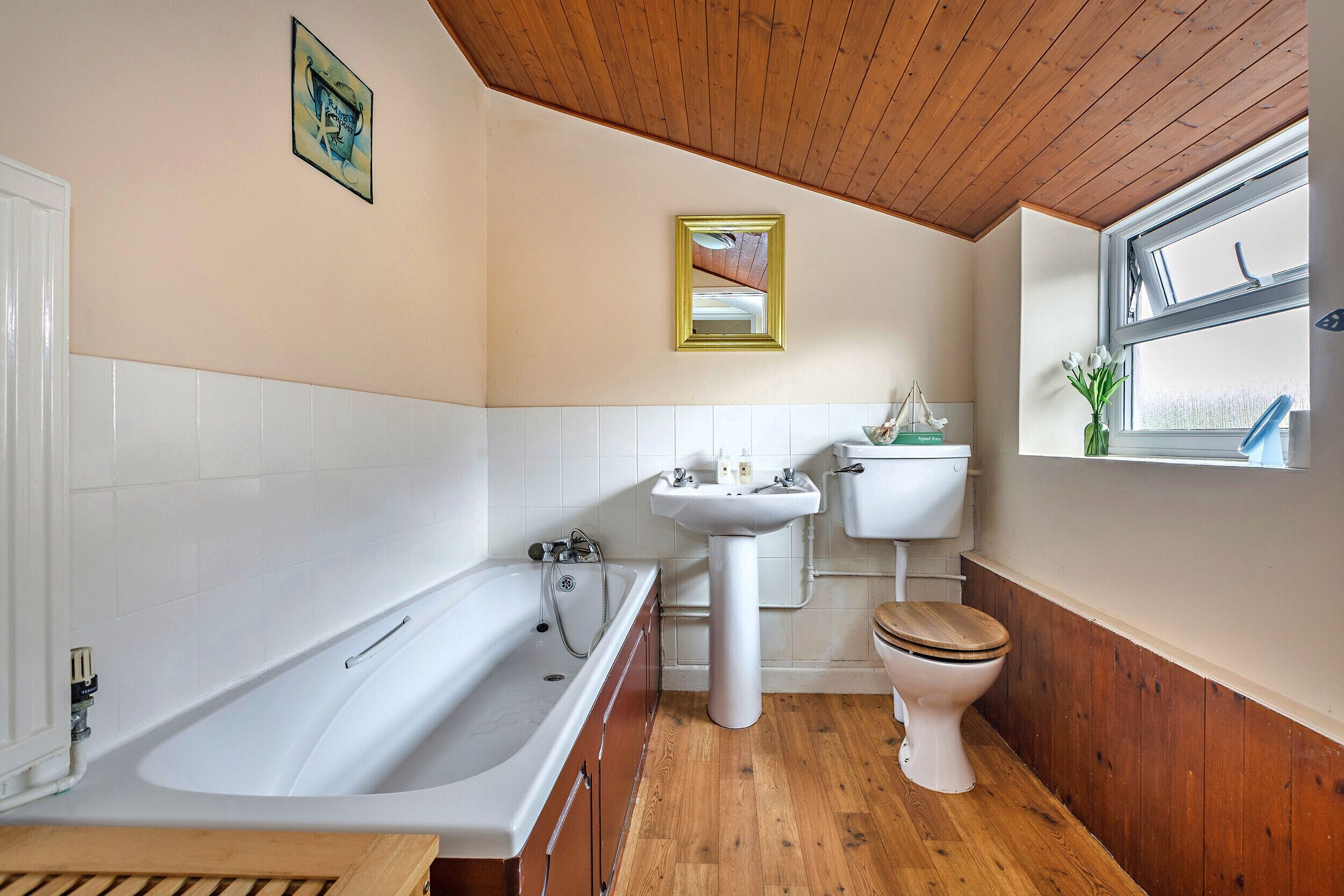 Une salle de bain avec une baignoire, un lavabo, des toilettes, un plancher en bois et une fenêtre donnant sur un beau paysage.
