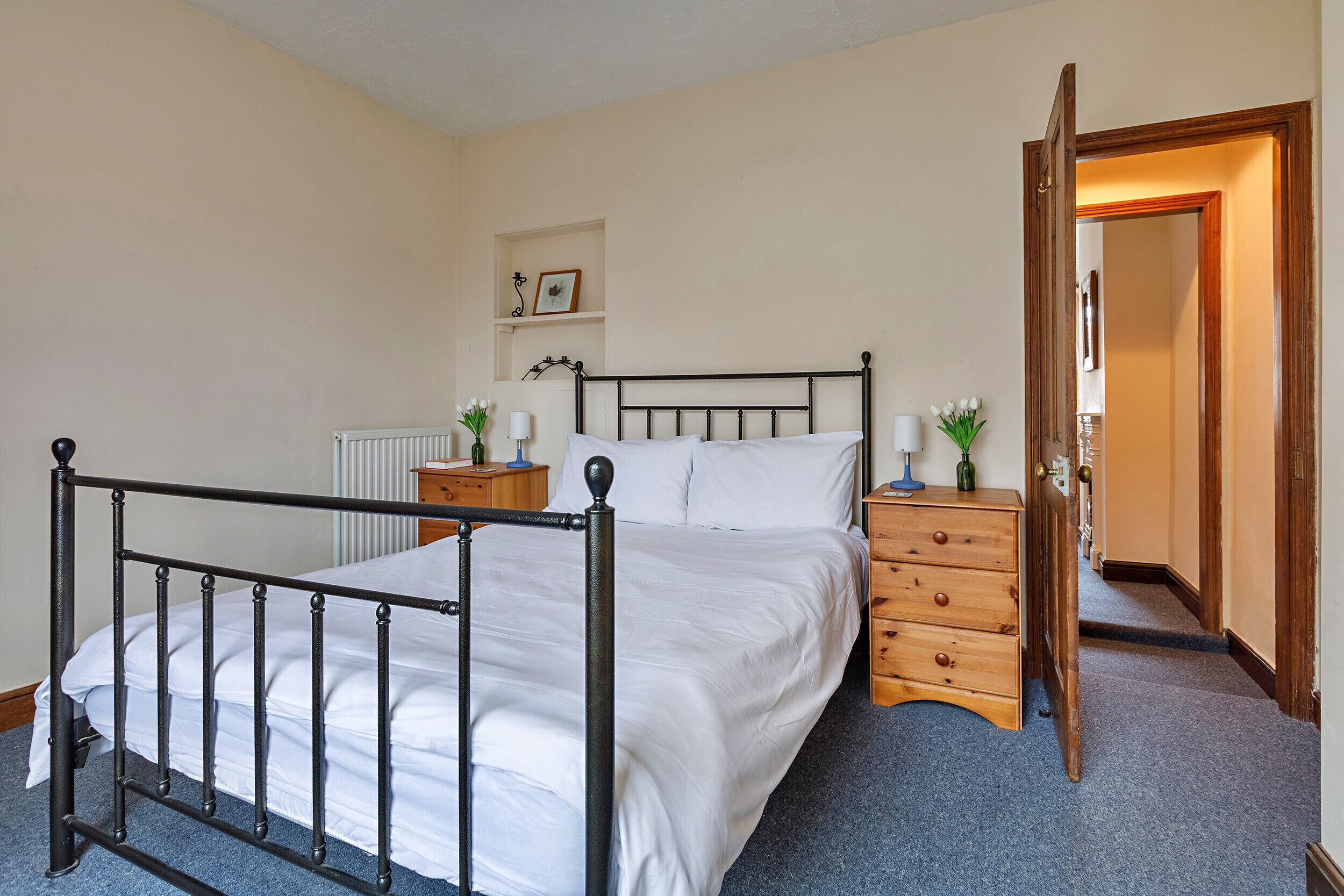A neatly made bed with white linens, a wooden nightstand with a lamp, and a dresser with drawers.