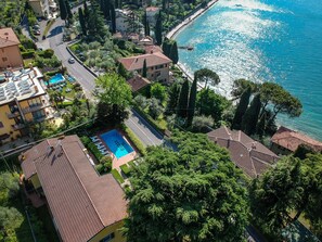 An aerial view of a coastal residential area with houses, a swimming pool, and a road.