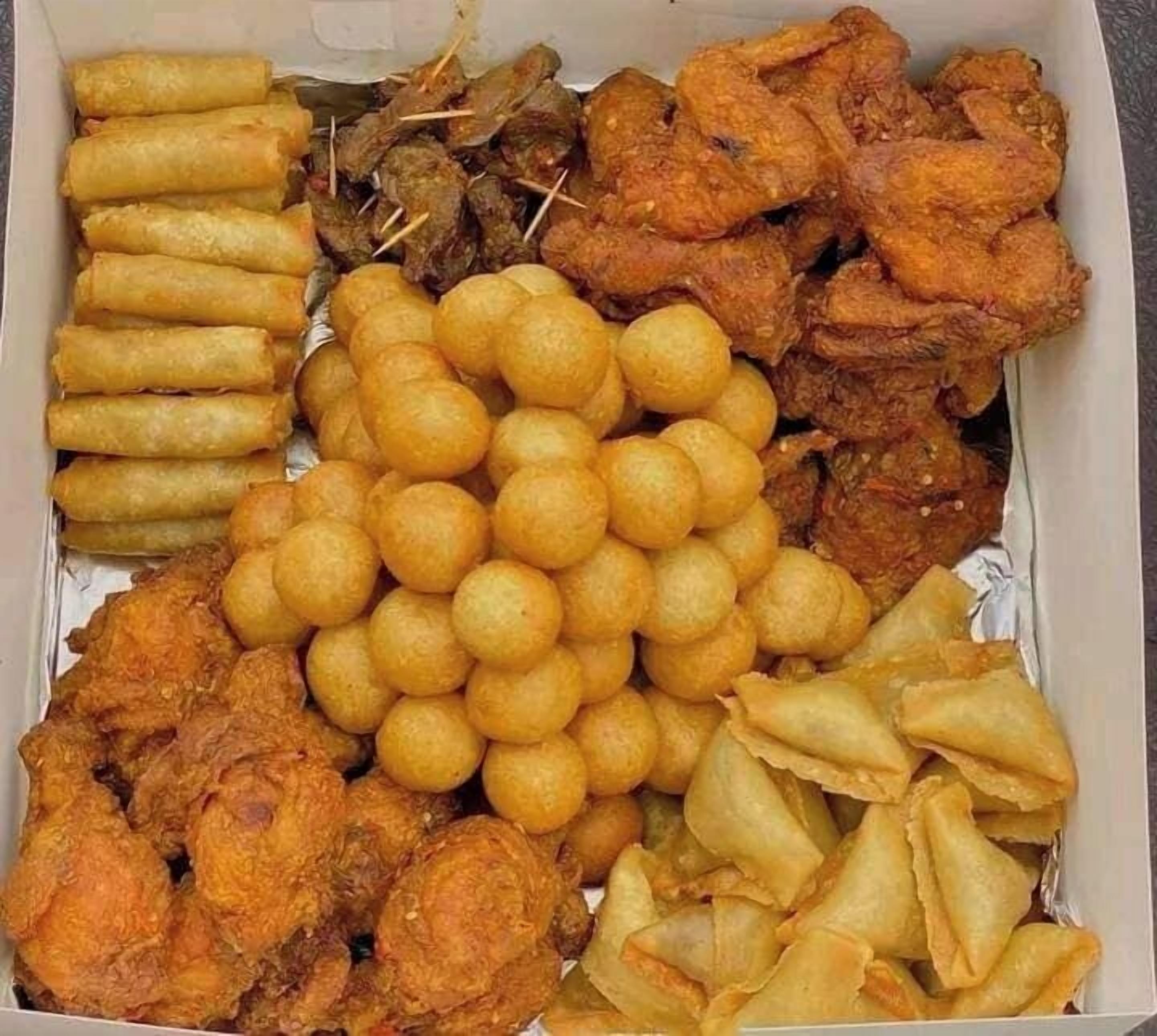 A box containing various fried foods including spring rolls, fried chicken, and fried dough balls.