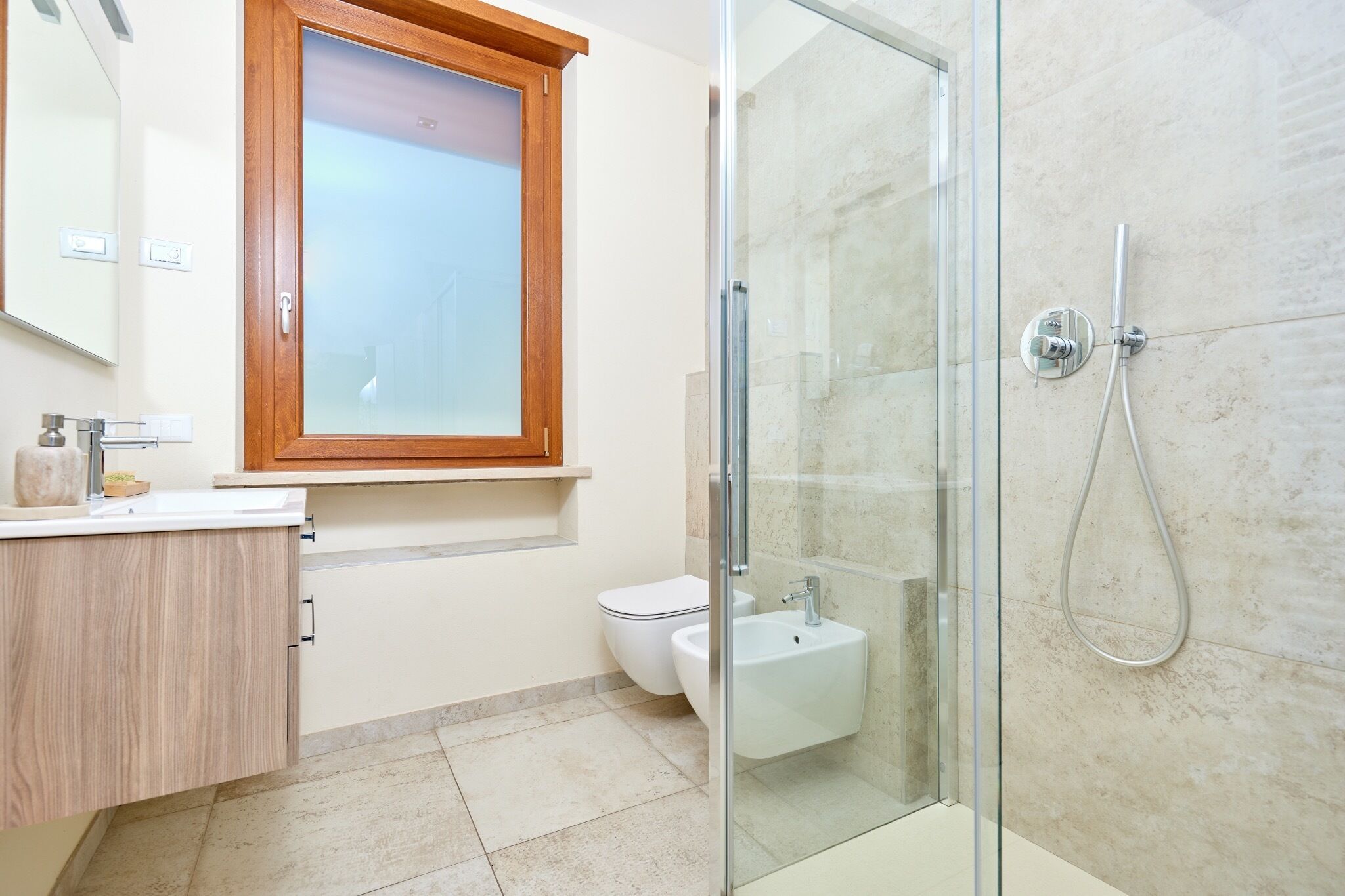 Un bagno moderno con box doccia in vetro, mobile lavabo in legno, WC bianco e specchio con cornice in legno.