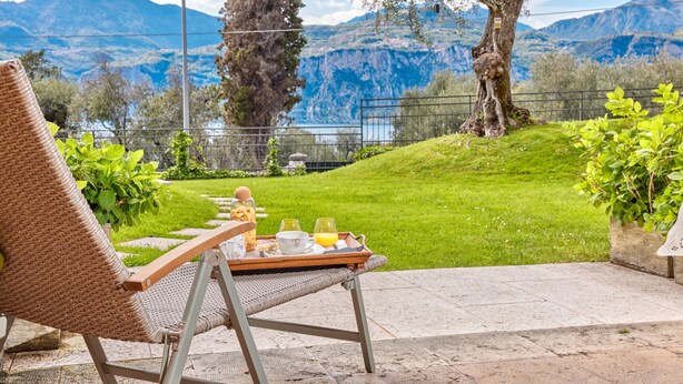 A wicker chair with a tray of breakfast items, a view of mountains and a lake.