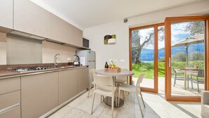 A modern kitchen with a dining area, large windows, and a view of the outdoors. - Residence Lilly-APT Jeneker- Garden with lake view, Residence Lilly - APT Jeneker - Giardino vista l (Malcesine)