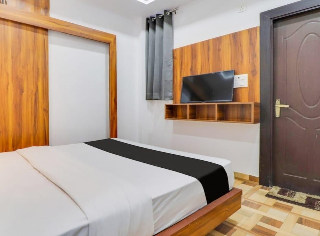 Un dormitori amb un llit, una televisió penjada a un panell de fusta, una porta i una finestra amb cortines.