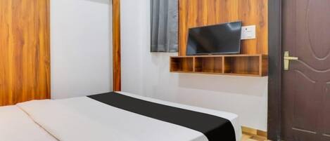 A bedroom with a bed, a TV mounted on a wooden panel, a door, and a window with curtains.