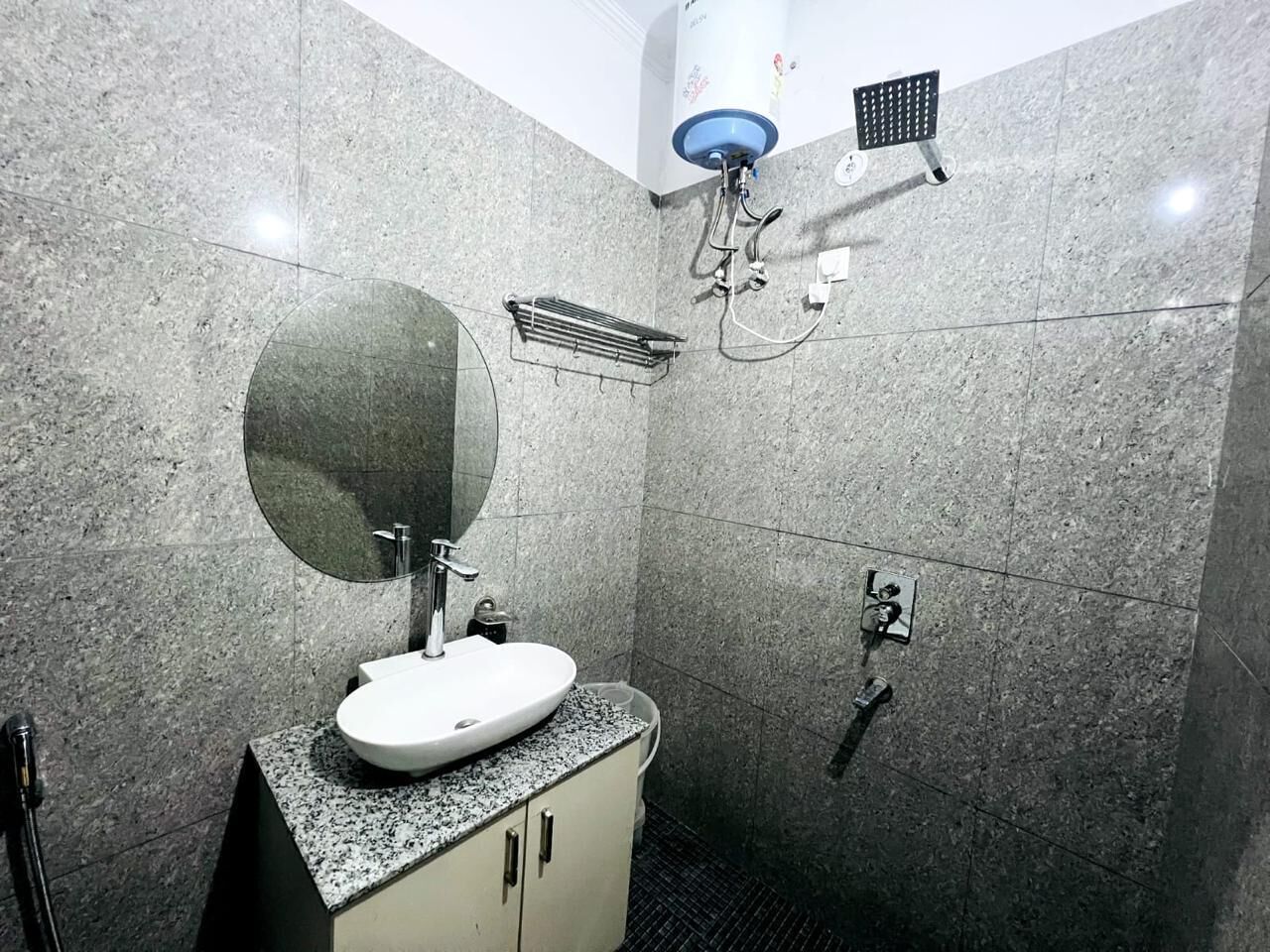 A modern bathroom with a granite countertop sink, a large mirror, a handheld showerhead, and a towel rack.