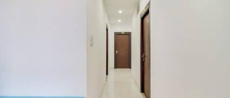 A clean, well-lit hallway with a blue bench on the left, a wooden door at the end, and a tiled floor.