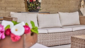 A wicker sofa with beige cushions against a brick wall, a wicker table with a vase of flowers, and a wicker chair. - Residence Lilly-APT Fefe- Balcony lake view, Residence Lilly - APT Fefe - Balcone vista lago (Malcesine)