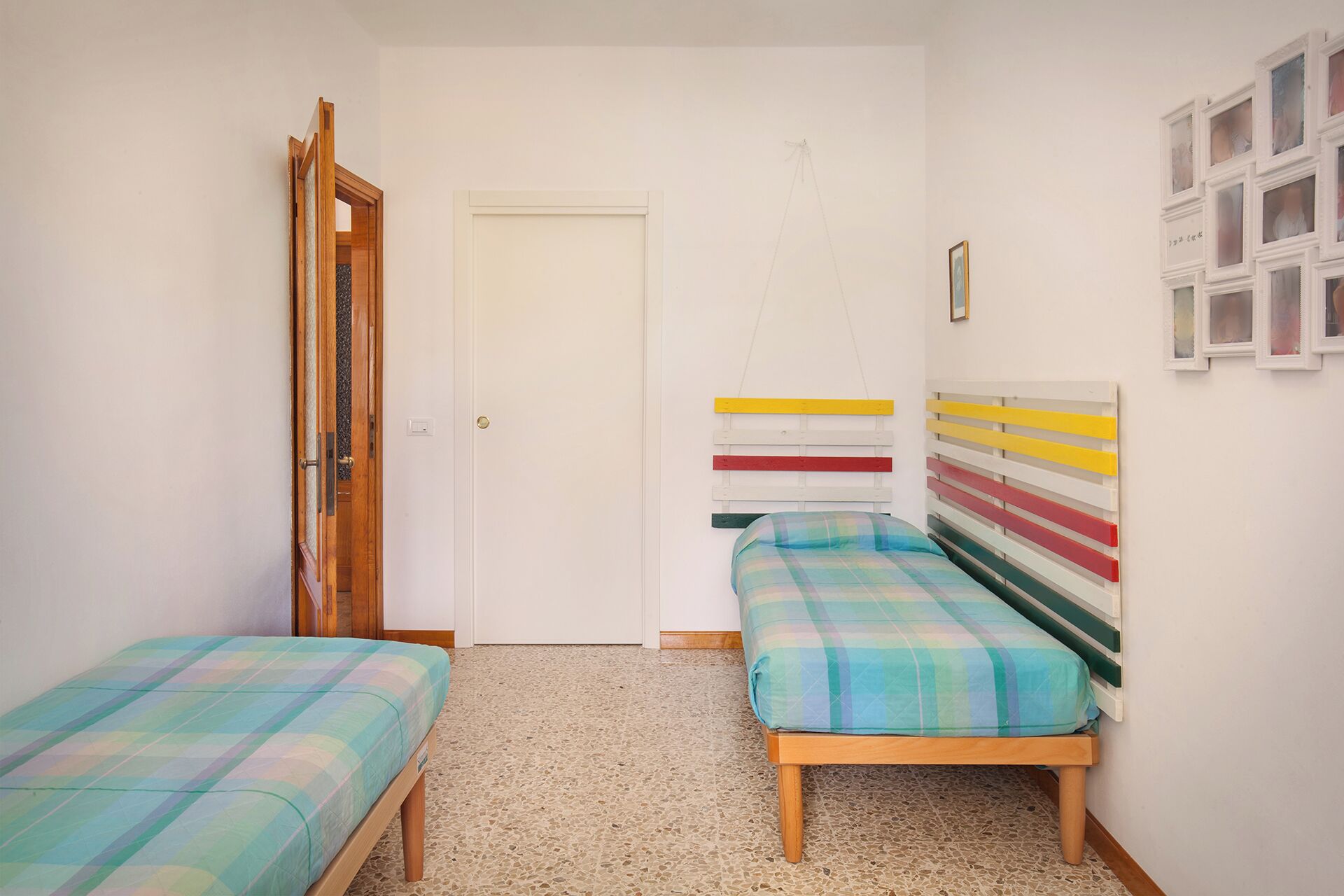 Une chambre avec deux lits simples, une porte en bois et une tête de lit colorée.