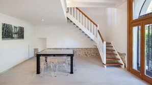 Une pièce spacieuse comprenant une table et des chaises, un escalier avec des marches en bois et une grande fenêtre donnant sur un paysage verdoyant.