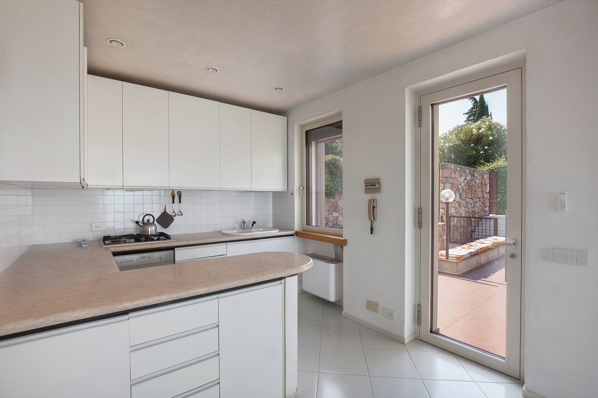 A modern kitchen with white cabinets, a gas stove, and a large window leading to a patio.