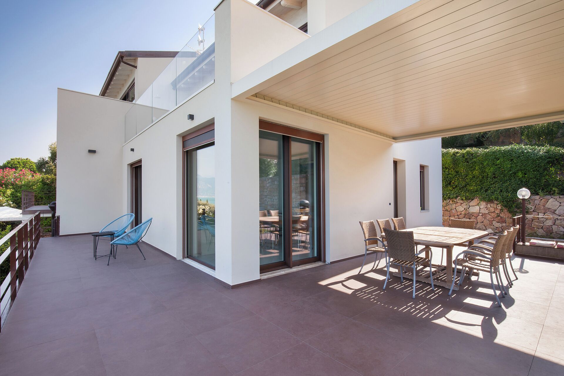 Un espace patio extérieur moderne, doté d’une table et de chaises, d’une chaise bleue et d’une porte vitrée donnant sur un espace intérieur.