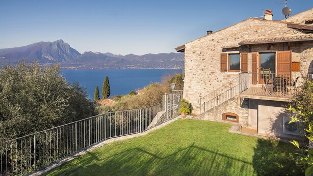 A stone house with a balcony overlooking a lake and mountains.