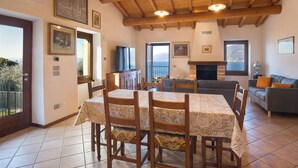 A spacious living room with a wooden ceiling, a fireplace, a dining area with a table and chairs, and a sofa.