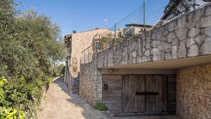 A narrow stone pathway leading to a rustic building with a wooden door and a stone wall.