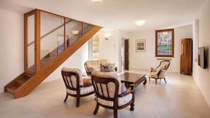 Un vaste salon agrémenté d’un escalier en bois, un coin repas avec des chaises à motifs floraux et une grande fenêtre donnant sur l’extérieur.