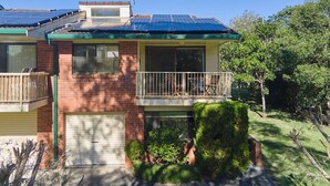 Une maison à deux étages, dotée de panneaux solaires sur le toit, d’un balcon avec des meubles d’extérieur et d’un jardin bien entretenu.