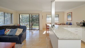 Une cuisine moderne dotée d’un grand îlot central, un coin repas avec une table et des chaises, et un salon avec un canapé et une table basse.