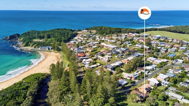 Vue aérienne d’un quartier résidentiel situé sur la côte, avec des maisons, une plage et une végétation luxuriante.