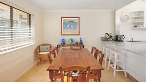 Un coin repas avec une table et des chaises en bois, un comptoir de cuisine avec des tabourets, et un tableau encadré au mur.
