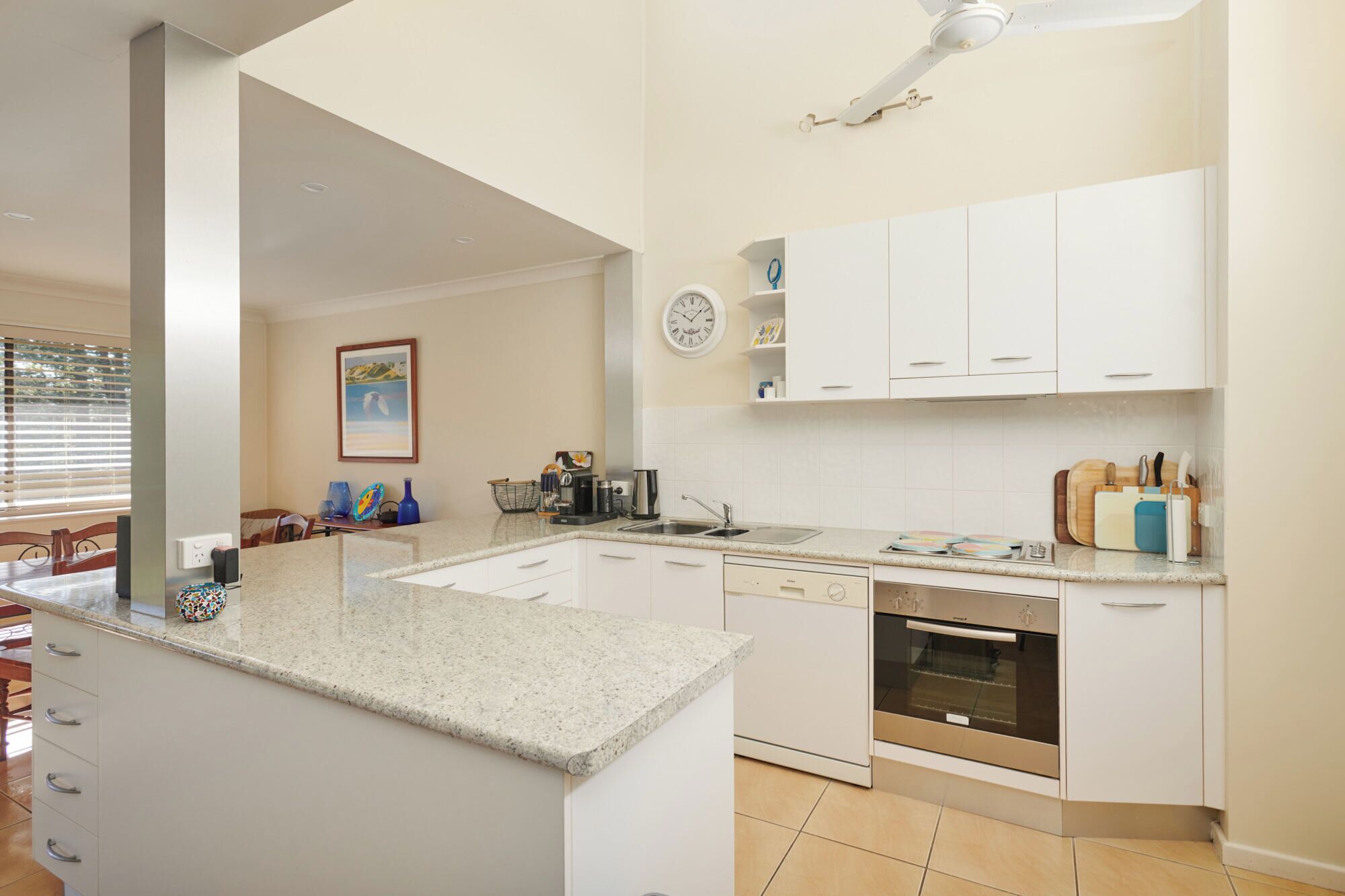 A modern kitchen with white cabinets, a granite countertop, a built-in oven, and a dining area with a table and chairs.