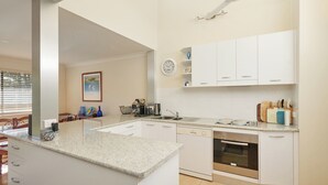 Une cuisine moderne avec des armoires blanches, un comptoir en granit, un four encastré et un coin repas comprenant une table et des chaises.